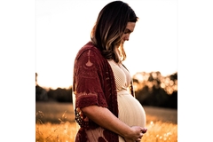 Image A pregnant woman looks at her belly while standing in a field of grain.